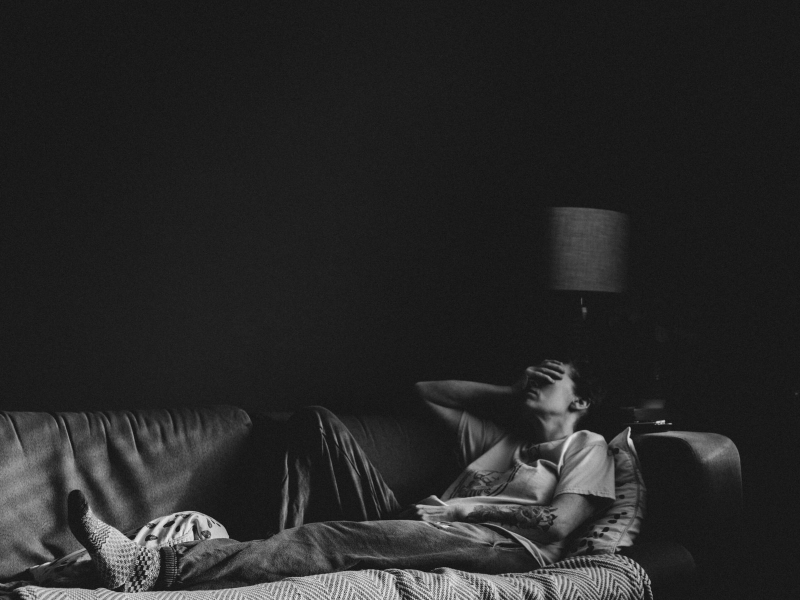 Personne allongée sur un sofa, la main devant le visage, fatiguée. Fatigue saisonnière.